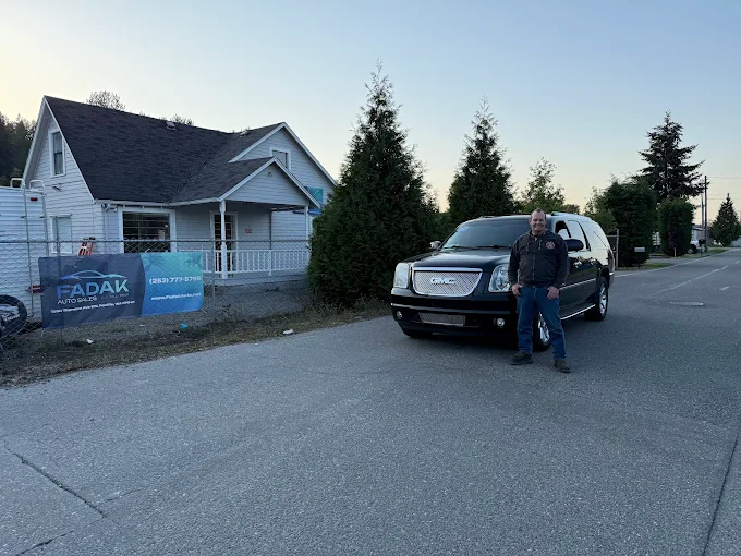 Black SUV parked near white house with Adak business sign