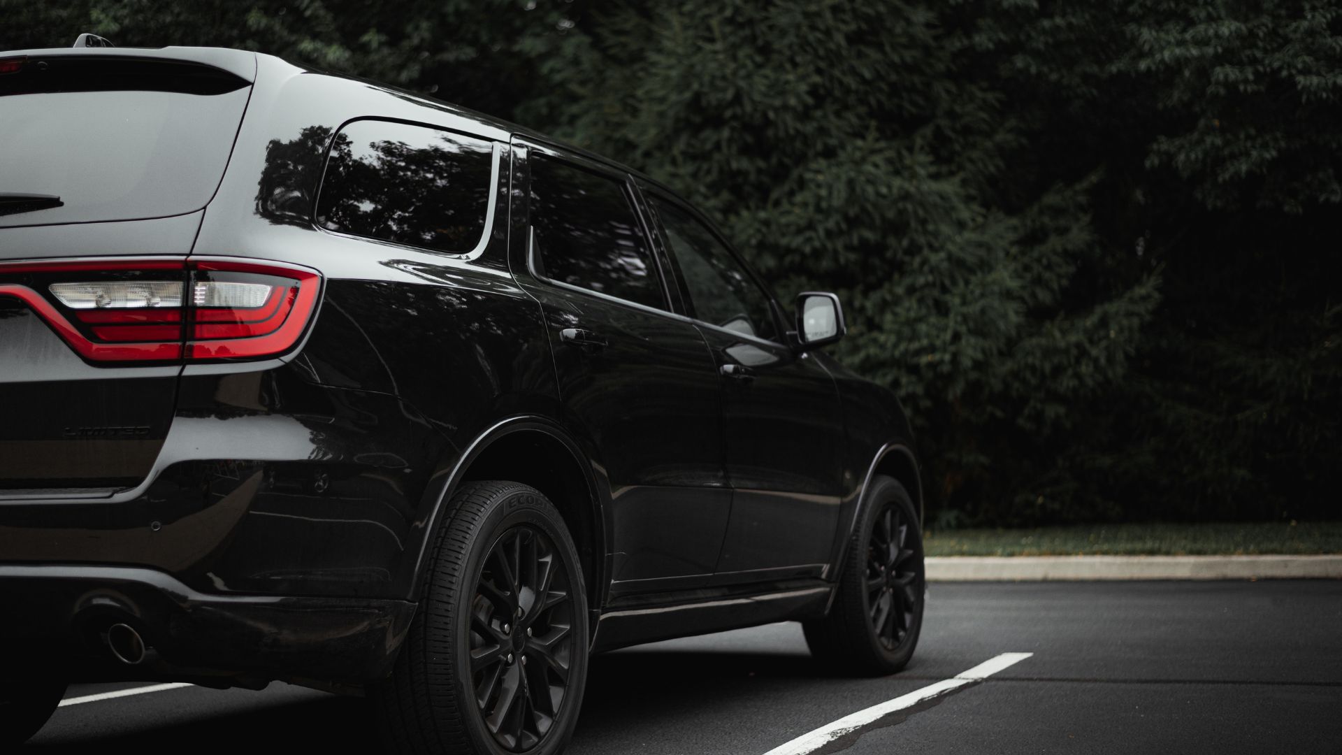 Black SUV parked on street with dark forest background