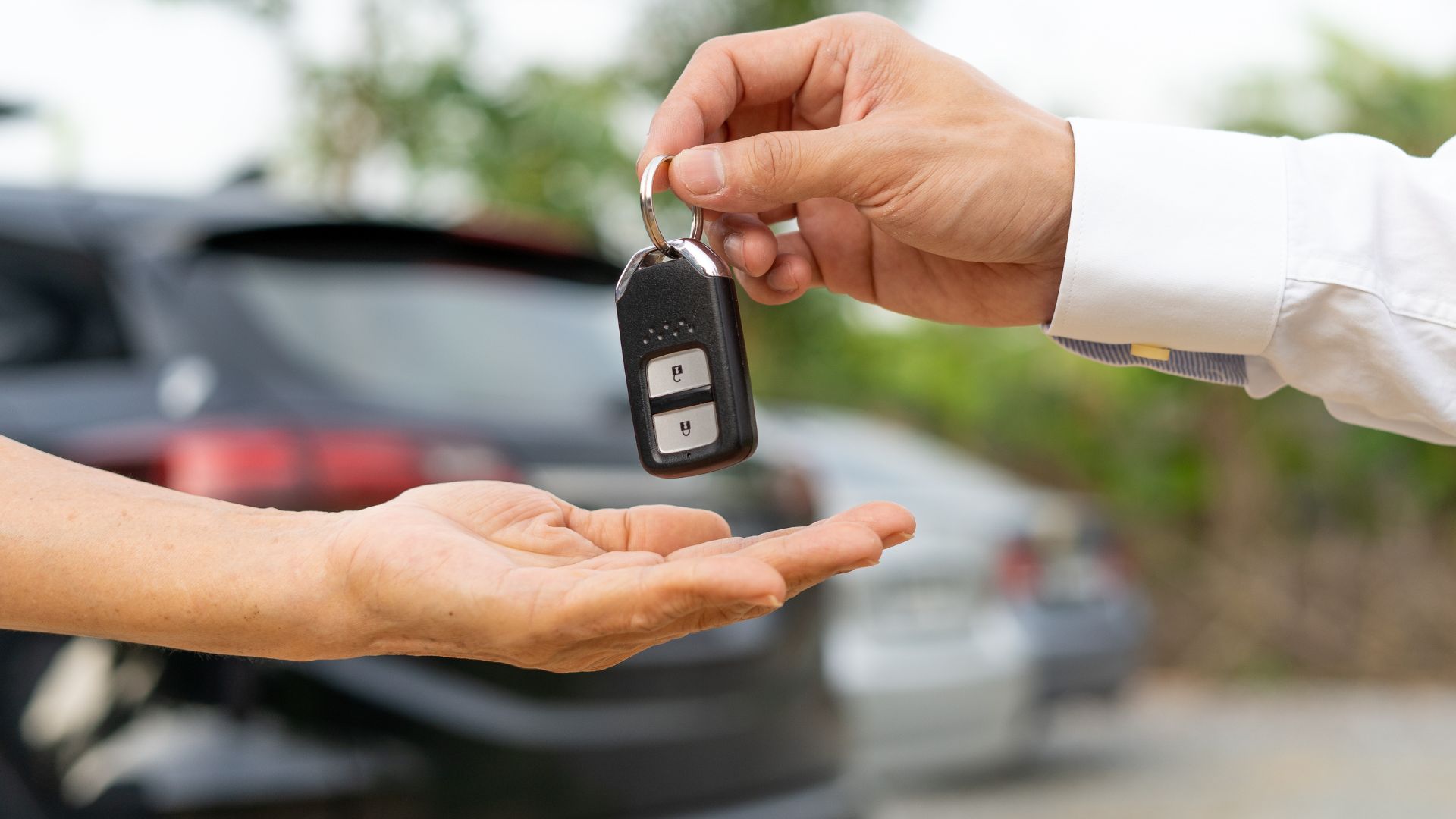 Car key being handed over between two people near a vehicle