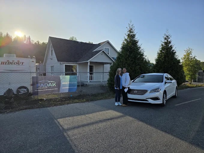White car parked beside house with two people at sunset